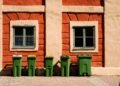 Green wheelie bins lined up outside a brick house