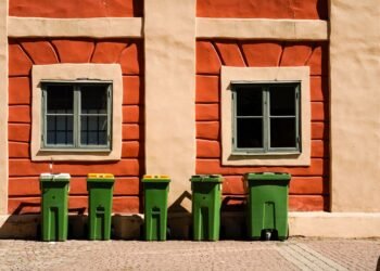 Green wheelie bins lined up outside a brick house