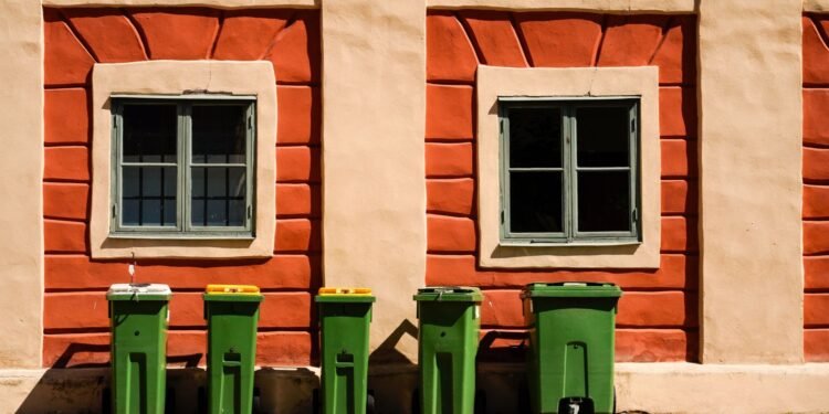 Green wheelie bins lined up outside a brick house