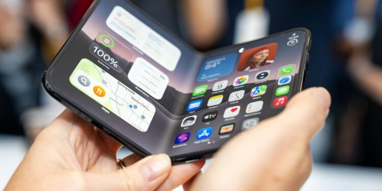 iPhone Duo foldable held open in two hands showing the iOS home screen